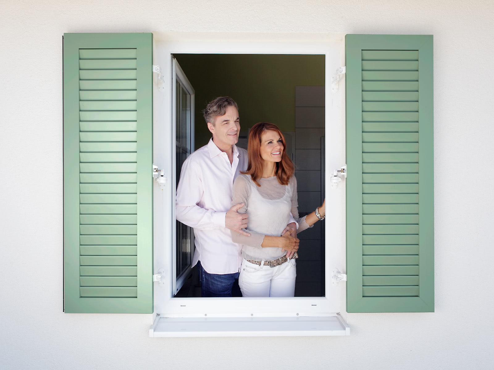 Bild: Paar steht an großem Fenster mit offenen Fensterläden und schaut nach draußen